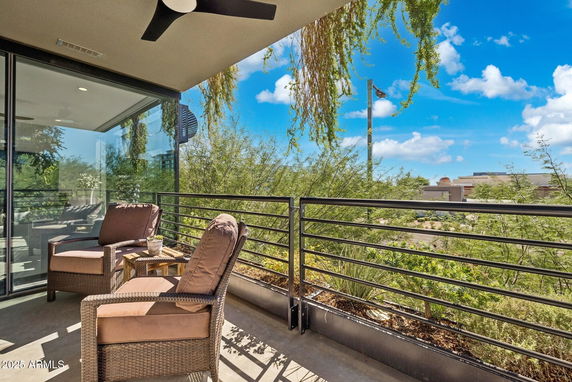 Balcony with two chairs and a small table overlooking trees and buildings.