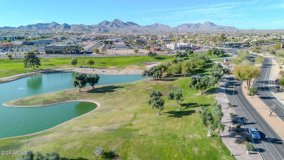 Wide angle view of a landscape featuring a pond, surrounding greenery, and distant mountains.