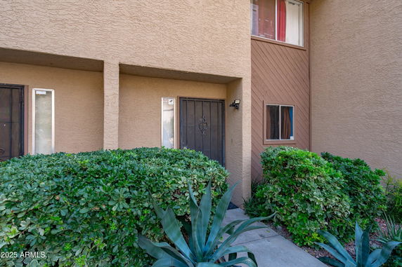 Front view of a building entrance with bushes and a secured door.