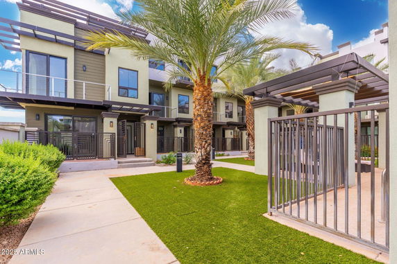 Front view of a modern multi-story house with a gated entrance and palm trees.