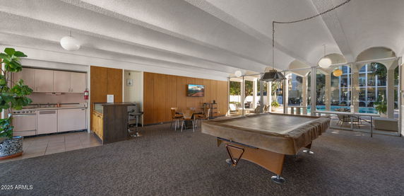 Interior view of a recreation room with a pool table, seating area, and large windows.