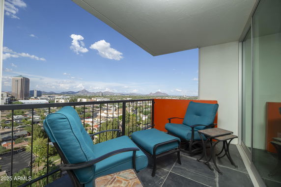 Balcony with chairs offering a panoramic view of cityscape and mountains.
