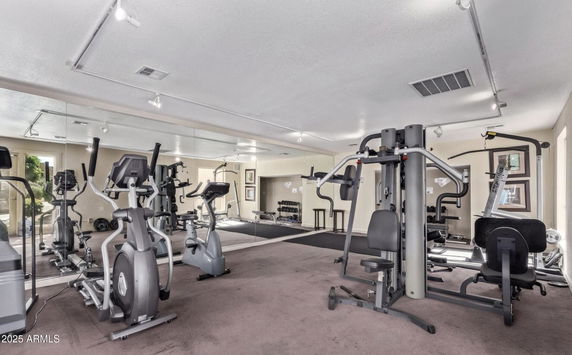 Indoor gym area with exercise equipment and mirrors on the walls.