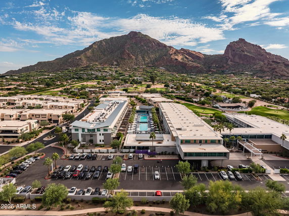 Aerial view of a large complex with multiple buildings, a central swimming pool, and parking areas, set against a mountainous backdrop.