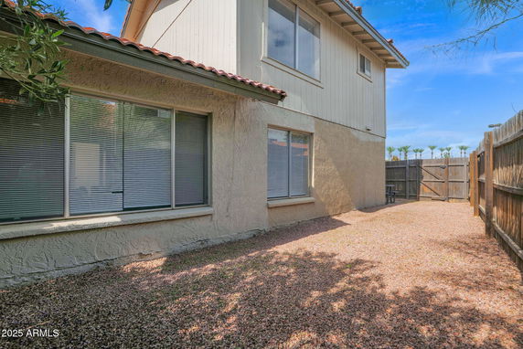 Side view of a two-story house with a gravel yard and wooden fence.