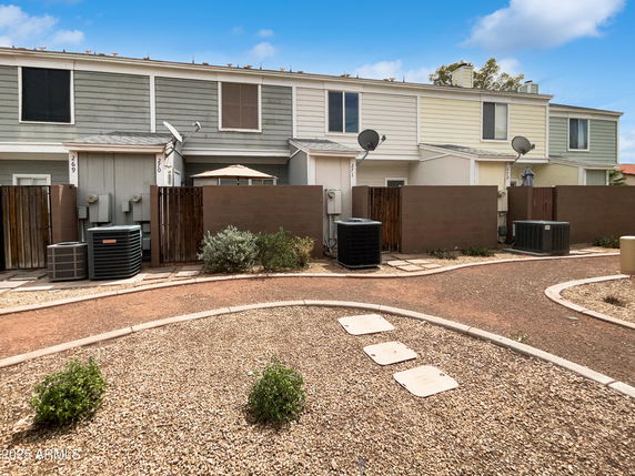 Front view of a row of two-story townhouses with fenced patios and air conditioning units.