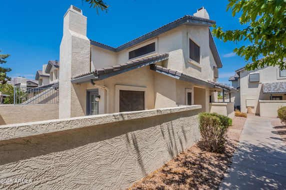Front view of a beige two-story house with a chimney and a surrounding wall.