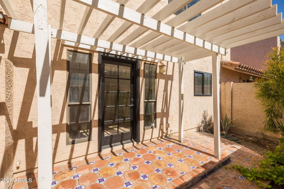 View of a house entrance with a tiled patio and wooden pergola.