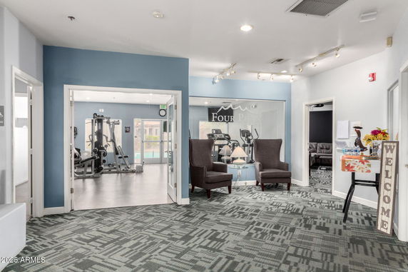 Interior view of a clubhouse with a gym area visible through a window.