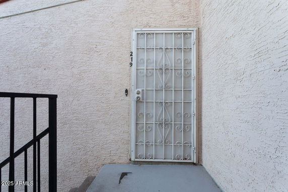 Front view of an exterior door with a decorative metal screen on a textured wall.