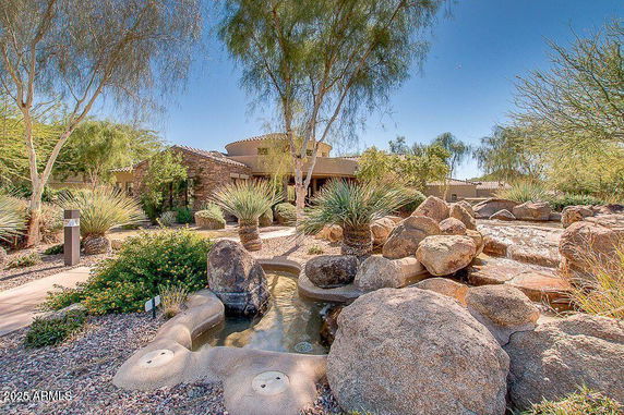 Front view of a house with stone and stucco exterior, surrounded by desert landscaping and rocks.