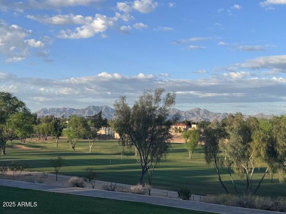 A panoramic view of a golf course with mountains in the background under a partly cloudy sky.