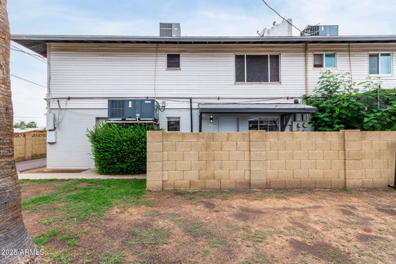 Side view of a two-story building with a brick wall and air conditioning units.