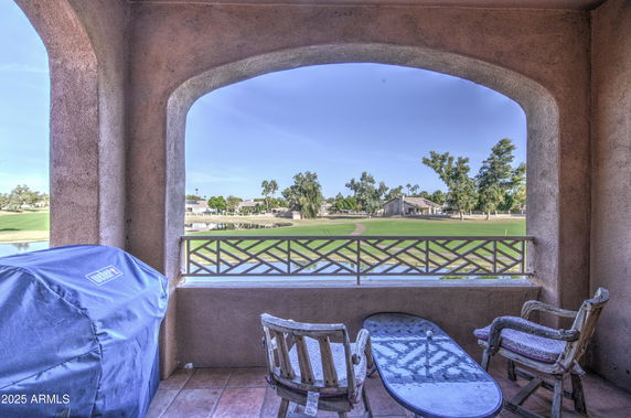A covered patio area overlooking a golf course with chairs and a barbecue grill on the side.
