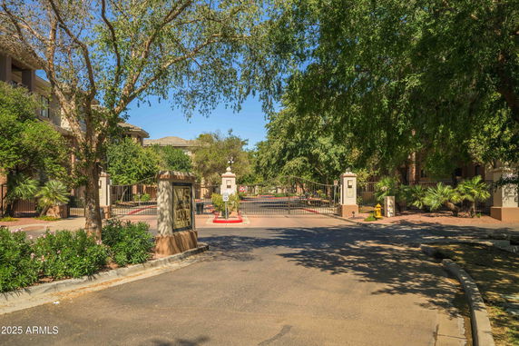 Front view of a gated residential complex with trees and paved entrance.