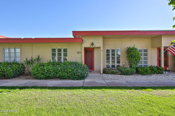 Front view of a single-story house with a red roof and bushes in front.