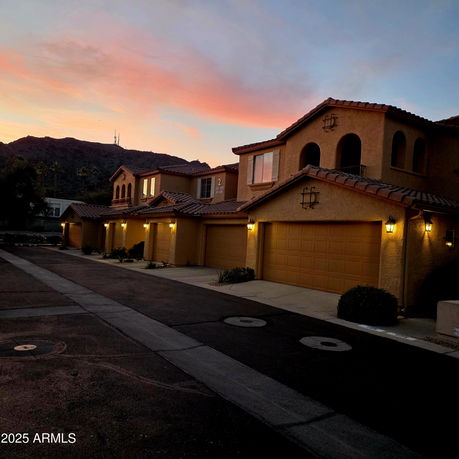 Front view of a row of two-story townhouses with garages at sunset.