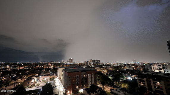 Panoramic view of a cityscape at night with illuminated buildings and cloudy sky.