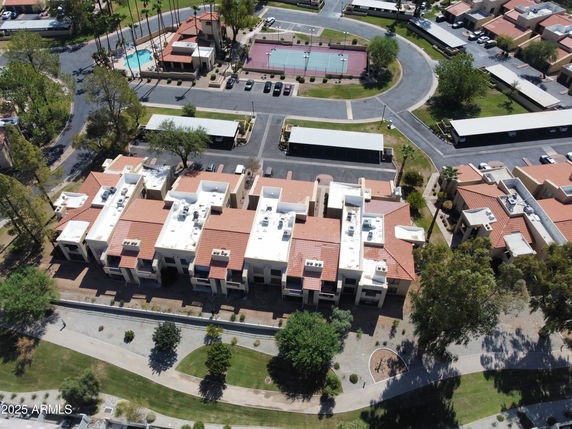 Aerial view of residential complex with flat and red-tiled roofs, surrounded by trees and pathways.