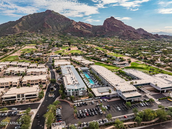 Aerial view of a complex of buildings surrounded by greenery with mountain backdrop.