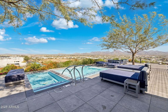 Panoramic view from a modern patio area with seating and a small pool overlooking a vast landscape and mountains.