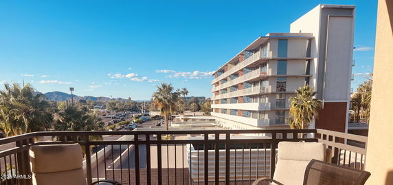 Balcony view overlooking a parking area, modern building, and distant mountains.