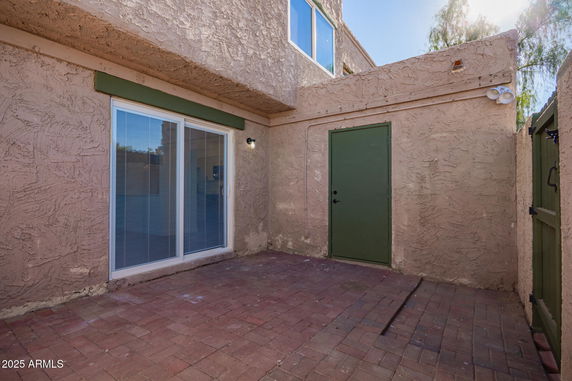 Exterior view of a building with textured walls, a sliding glass door, and a green door next to a fenced area.