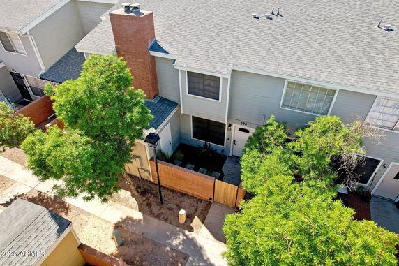 Aerial view of a two-story townhouse with a brick chimney and fenced front yard.