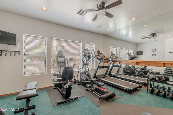 Home gym with exercise equipment, mirrors, and a ceiling fan.