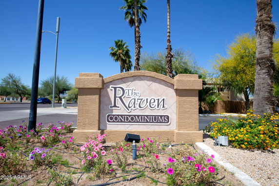 Entrance sign of The Raven Condominiums with landscaped area and palm trees.