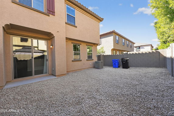 Rear view of a two-story house with a gravel yard and fenced perimeter.