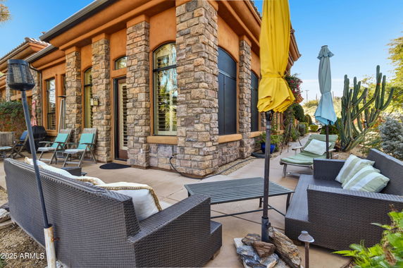 Front view of a house with stone pillars and a patio area with outdoor seating and umbrellas.