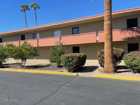 Front view of a two-story building with a balcony and palm trees in the background.