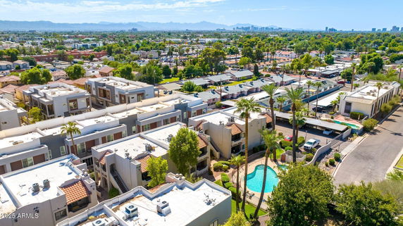 Wide-angle view of a residential area with multiple buildings and a swimming pool, surrounded by trees.