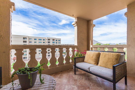 Balcony view with seating area overlooking adjacent buildings and distant mountains.