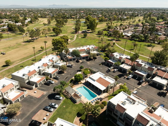 Aerial view of a residential complex with multiple buildings, a swimming pool, and surrounding green areas.