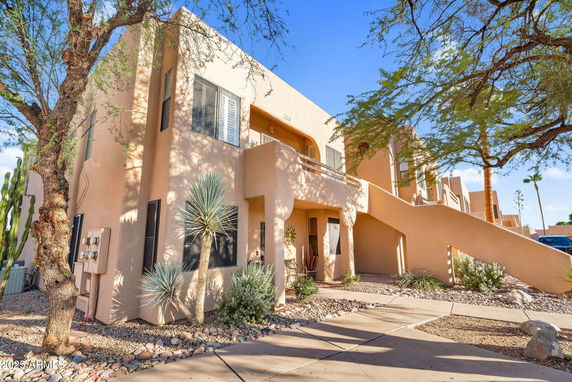 Front view of a two-story building with an external staircase and desert landscaping.