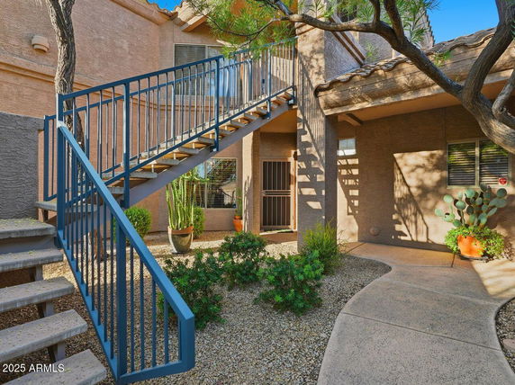 Front view of a two-story building with outdoor staircase and desert landscaping.