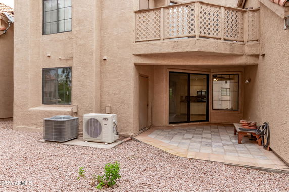 Rear view of a house with a patio area and air conditioning units.