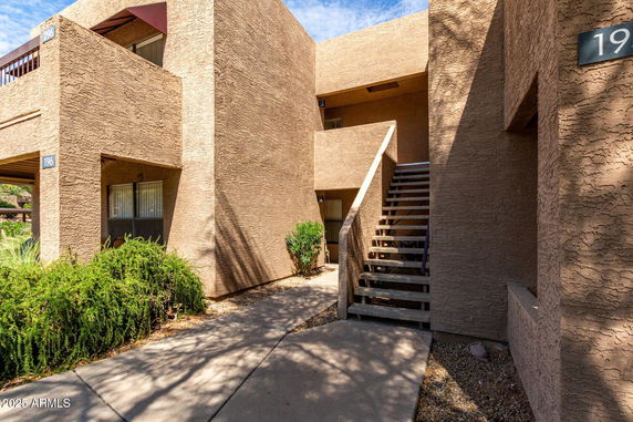 Front view of a two-story building with textured beige walls and exterior stairs.