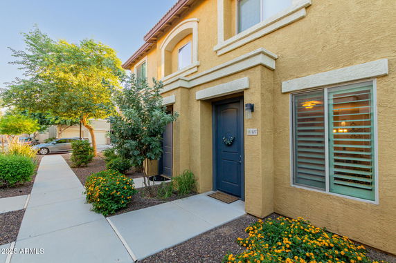 Front view of a house with a beige facade and dark doors located on a landscaped pathway.