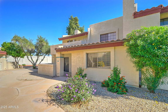 Front view of a two-story house with a slightly arched roof and surrounding shrubs.