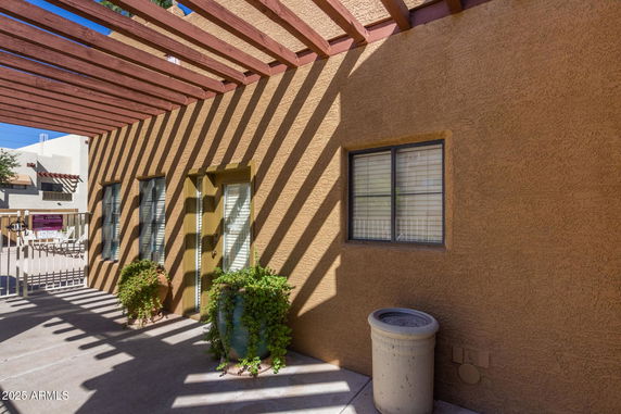 Side view of a building with wooden pergola and potted plants.