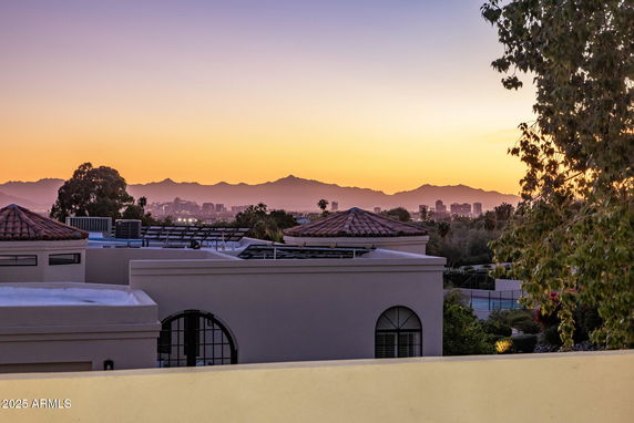 Panoramic view of the city skyline and mountains at sunset, with rooftop structures in the foreground.