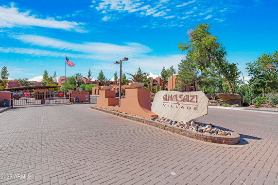Entrance to a residential complex with a sign that reads 'Anasazi Village' and an American flag nearby.