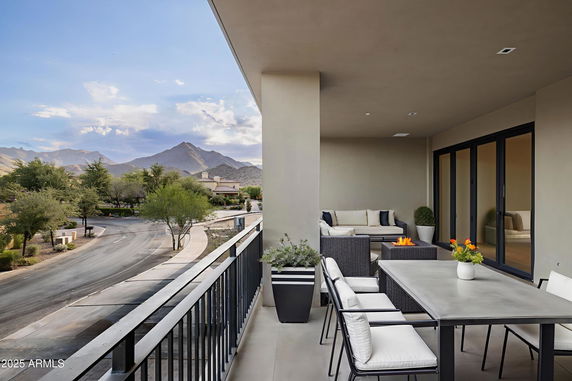 Covered balcony with outdoor seating and dining area, overlooking a street and distant mountains.