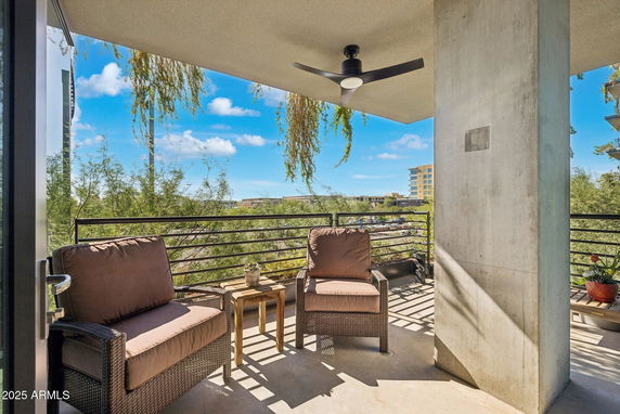 Balcony view from a building with outdoor seating and railing, overlooking trees and other buildings.