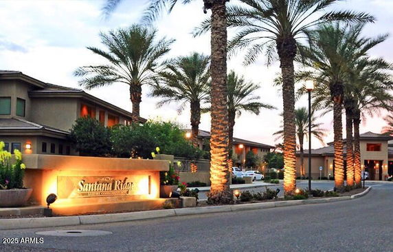 Front view of a residential building with palm trees and illuminated sign at entrance.