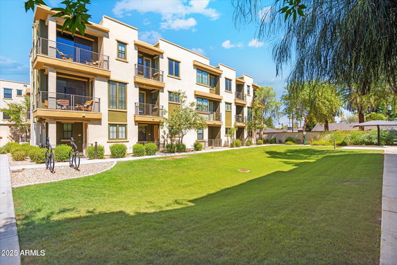 Front view of a multi-story residential building with balconies and green lawn area.