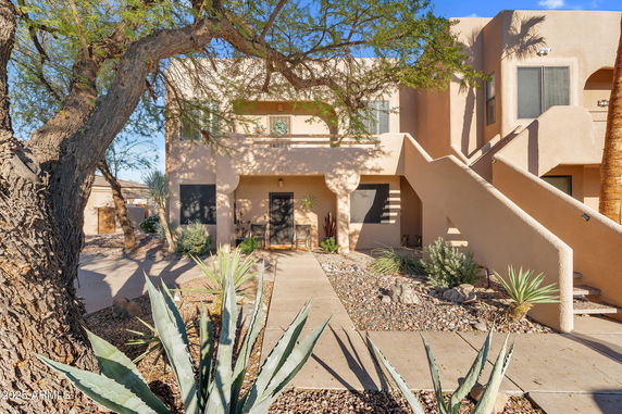Front view of a two-story adobe-style house with outdoor stairs and a small porch.